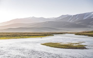 Yüksek dağ manzarası, dağlarda bir nehir bir dağ vadisinde yeşil çayırlar arasında dağların arka planına karşı akar, arka plan için Pamir Dağları 'ndaki manzara