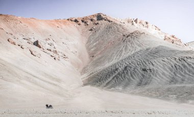 Tacikistan 'daki Tien Shan dağlık arazisindeki Pamir Otobanı' nda bir motosiklet, dağ zirvelerinin arka planına karşı.