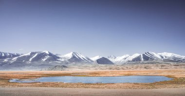 Yüksek dağ manzarası, dağlarda bir nehir bir dağ vadisinde yeşil çayırlar arasında dağların arka planına karşı akar, arka plan için Pamir Dağları 'ndaki manzara