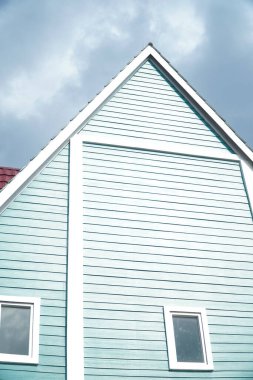 Gable çatısı ve bulutlu arka planı olan yeşil antika bir ev.