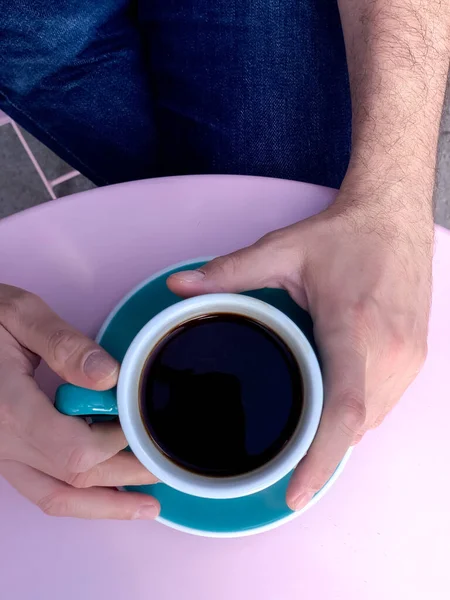 Man is drinking americano coffee. Mans hands holding coffee mug.Morning coffee in tiffany color ceramic mug with saucer on pink table. High quality photo