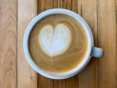 Tahta bir masada bir fincan kahve. Ahşap arka planda bir kupa düz beyaz kahve. Kahve sanatı. Kalp çiçeği şekilli latte sanatı. Uzayı kopyala Yüksek kalite fotoğraf