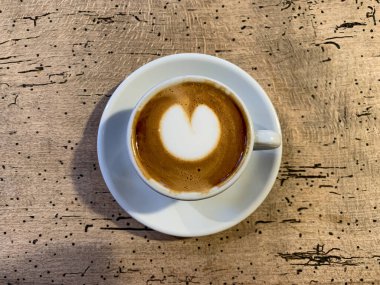 Tahta bir masada bir fincan kahve. Ahşap arka planda bir kupa düz beyaz kahve. Kahve sanatı. Kalp çiçeği şekilli latte sanatı. Uzayı kopyala Yüksek kalite fotoğraf