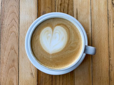 Tahta bir masada bir fincan kahve. Ahşap arka planda bir kupa düz beyaz kahve. Kahve sanatı. Kalp çiçeği şekilli latte sanatı. Uzayı kopyala Yüksek kalite fotoğraf
