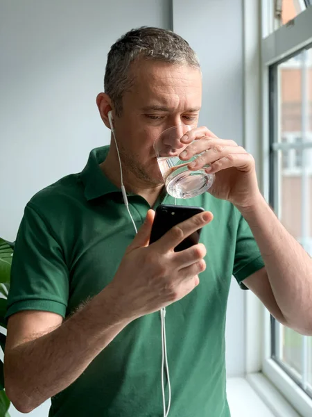 Middle aged man is talking on phone and drinking water. Video call. Middle aged man is talking on phone with friends or family, video call, watching video or checking news on social media. Staying at