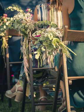 Bir buket çiçeğin düğünde bir sandalyeyi dekore etmesi ve tören sırasında misafirlerin oturması.