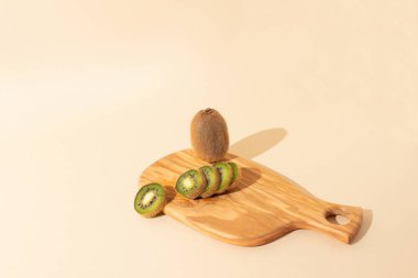 Açık bej arka planda taze kesilmiş kivi ile ahşap tabak. Düz yatıyordu.