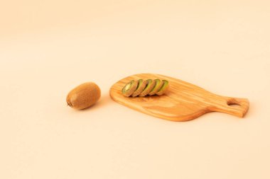 Açık bej arka planda taze kesilmiş kivi ile ahşap tabak. Düz yatıyordu.