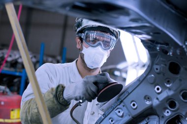 Koruyucu ekipman giyen genç adam araba faktöründe çalışıyor.