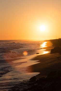 Gün batımında sıcak bir gökyüzünün dikey görüntüsü. Deniz dalgaları ve ıssız sahil de dahil.