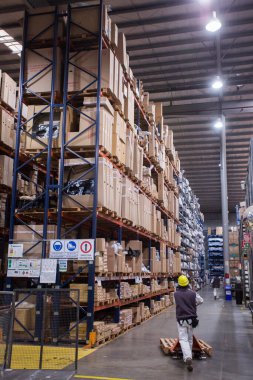 İş yerindeki adamlar, koruyucu giysiler giyiyorlar, depoda kutularla uğraşıyorlar.