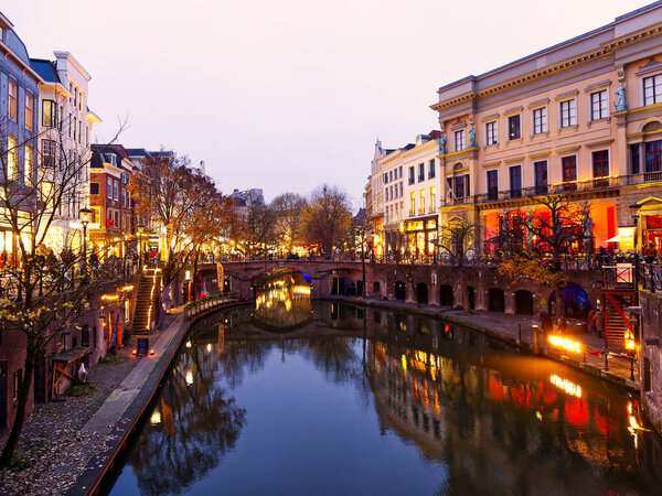 Beautiful canals cityscape under warm lights during a misty and cloudy winter evening, Utrecht, Netherlands 