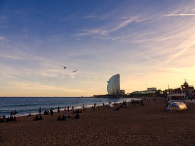 Barselona, İspanya - 20 Kasım 2022: Barceloneta, gün batımında W Barcelona Oteli manzaralı. Kumsal insanlarla dolu.. 