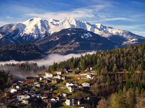 Alpine landscape snowcapped mountain view with low clouds at dawn from Trin, Switzerland. Rays of sunshine casting over the village and mountains.