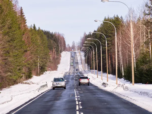 stock image Asphalt highway with cars through the forest in a sunny winter day. Vanishing point. 