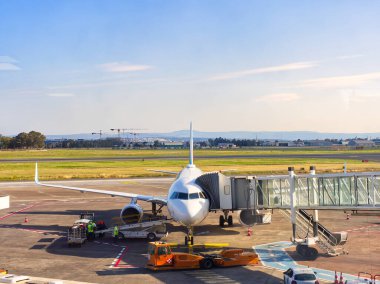 Jet Bridge 'e park edilmiş ticari uçak. Yer ekibi ve ekipman pistte.