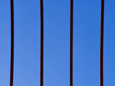 Koyu mavi gökyüzü arkaplanıyla çelişen dikey metal çubukların minimalist görüntüsü