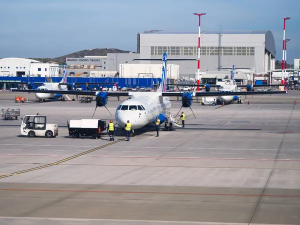 Havaalanı binaları ve arka planda diğer uçaklarla birlikte pistte turboprop uçağı.