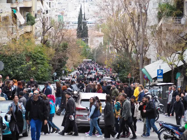 Atina, Yunanistan - 28 Şubat 2025: Tarihi bir kent ortamında eski binalar ve ağaçların arasında yürüyen çeşitli insanlarla dolu kalabalık bir cadde. Tempi tren kazasını protesto etmek