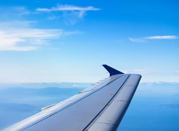 Mavi gökyüzü ve aşağıdaki dağınık bulutlarla, uçuş sırasında uçak kanadının görüntüsü