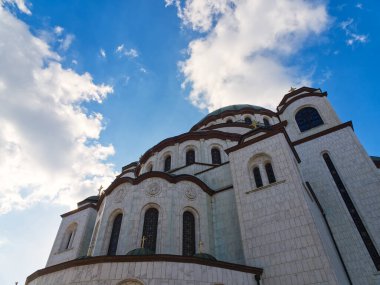 Kubbeli çatısı ve bulutlu bir gökyüzünün altında beyaz duvarları olan büyük bir Ortodoks kilisesinin dış görünüşü. Saint Sava Kilisesi, Belgrad