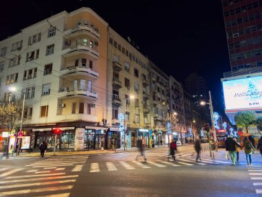 Belgrad, Sırbistan - 10 Ocak 2025: Tarihi bina, yayalar ve gece yoğun yaya geçidi ile aydınlık sokak köşesi