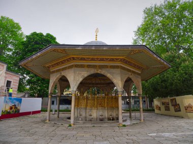 Ağaçlarla çevrili bir bahçe ortamında altın süslemelerle süslü altıgen fıskiyeler.