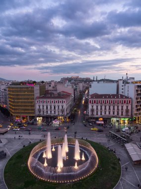 Atina, Yunanistan - 5 Nisan 2025: Atina şehir merkezinin alacakaranlıktaki havadan görünüşü, dairesel aydınlatılmış çeşme ve tarihi binaların yer aldığı