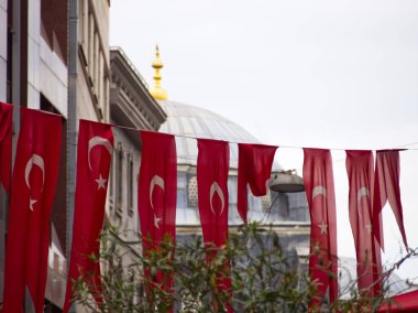 Beyaz kubbesi ve altın kulesi olan bir caminin önünde hilal ve yıldız asılı kırmızı Türk bayrakları