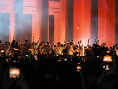 Atina, Yunanistan - 3 Mayıs 2025: Atina Şehir Festivali 'nde 2025 yılındaki sütunlara karşı kollarını kaldırıp turuncu ışıkta yıkanan insanlar konserde siluetler