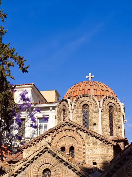 Panaghia Kapnikarea Kilisesi 'nin kubbeli çatısı, kemerli pencereleri ve Ermou Caddesi' nin ortasında mor jakaranda çiçekleri var. Atina, Yunanistan