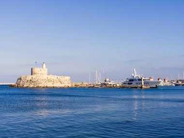 Deniz feneri ve limanın içinde sakin mavi suları olan modern yatları olan Rhodes Adası kalesi. Yunanistan