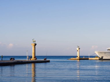 Rodos, Yunanistan - 26 Nisan 2025: Meçhul ve Geyik heykelleri ile iki sütun sakin mavi deniz ve açık gökyüzü ile bir limanın girişini işaret ediyor