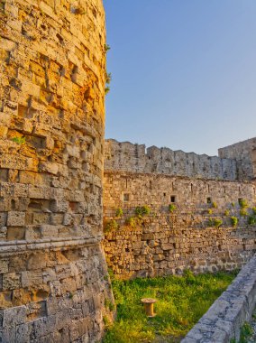 Altın güneş ışığı, Rodos 'taki ortaçağ taş tahkimatlarını aydınlatıyor. Çimenli duvarları ve çimenli hendek bölgesi olan eski bir kasaba.