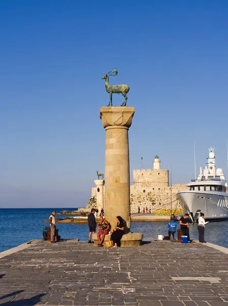 Rodos, Yunanistan - 26 Nisan 2025: Rodos limanındaki sütununda İkonik geyik heykeli, arka planda ortaçağ kalesi ve yatıyla