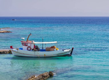 Akdeniz 'in berrak turkuaz sularında kayalık kıyılara yakın bir yerde demirli küçük beyaz balıkçı teknesi. Koufonisia Adaları, Kiklad Adaları, Yunanistan