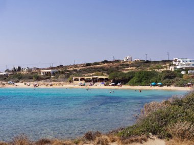 Güneşli bir günde turkuaz bir körfez manzarası, kumsala gidenler ve sahil binaları. Koufonisia Adaları, Kiklad Adaları, Yunanistan