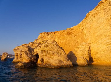 Dramatik altın kireçtaşı kayalıkları ve kaya oluşumları berrak gökyüzünün altındaki durgun mavi sulardan yükseliyor. Koufonisia Adaları, Kiklad Adaları, Yunanistan