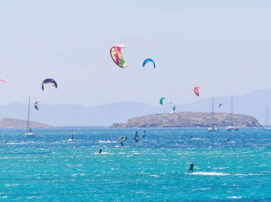 Çok renkli uçurtmalar gökyüzünü turkuaz bir denizin üstünde, uçurtmacılar rüzgarın ve dalgaların tadını çıkarıyorlar. Paros Adası, Yunanistan