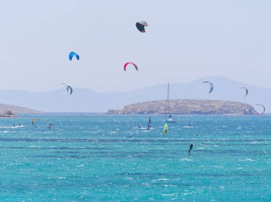 Çok renkli uçurtmalar gökyüzünü turkuaz bir denizin üstünde, uçurtmacılar rüzgarın ve dalgaların tadını çıkarıyorlar. Paros, Yunanistan