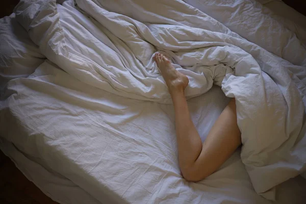 优雅的女性腿从床上的白色毛毯下向外张望 — 图库照片