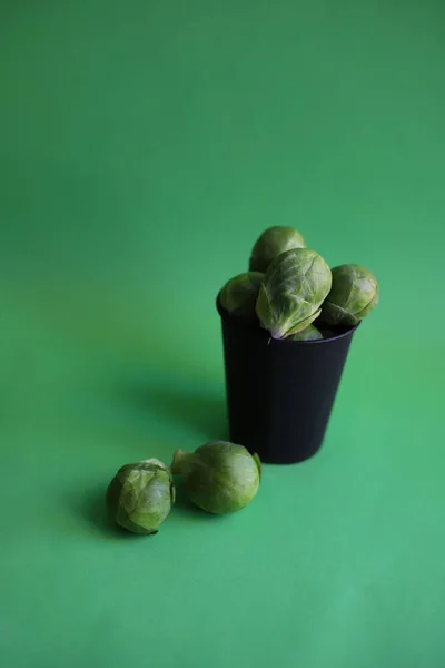 Brussels sprouts juicy healthy green cabbage is poured into a black craft glass on a bright green background with water drops. for shop labels intro banners recipes