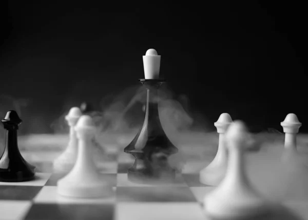 在比赛的棋盘上 有一块黑色皇后的棋子 周围是黑烟熏天的白爪 用来做横幅 比赛海报 — 图库照片