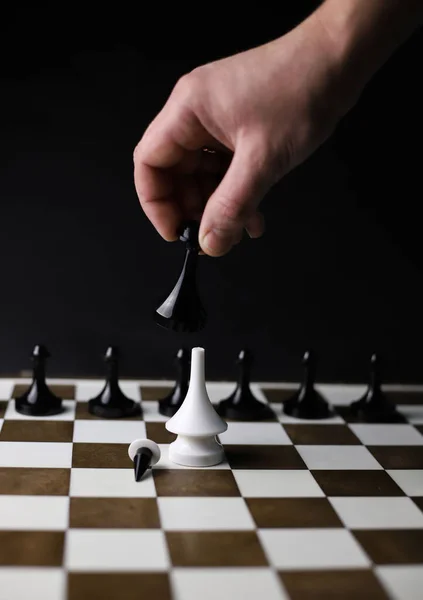 on a game chessboard, a chess black rook piece in hand beats a white bishop surrounded by black pawns. for banners, signage, labels, flyers, tournament posters