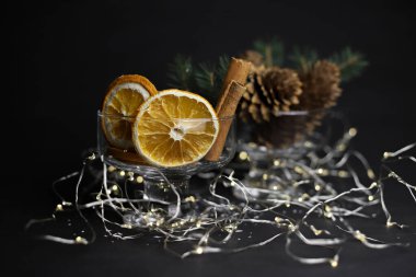 Karanlık bir arka planda, portakallar, tarçın konileri, bir çelenk ve bir Noel ağacı ile birlikte iki şeffaf bardak. kart davetleri için etiketler takvimi