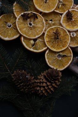 Kurutulmuş portakal kozalakları tarçın köknar dalları ve yıldız anasonu ahşap doğal sopaların üzerine güzelce serilmiş koyu bir arka planda noel süslemesi. Kart takvimi etiketleri, işaret davetiyesi ilanları için