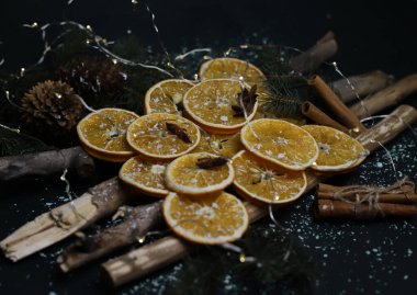 Kurutulmuş portakal kozalakları tarçın köknarı dalları ve yıldız anasonu ahşap doğal sopaların üzerine serilmiş kar ve çelenklerle kaplı karanlık bir arka planda Noel süslemesi. Kart takvimi etiketleri, işaret davetiyesi ilanları için