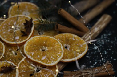 Kurutulmuş portakal kozalakları tarçın köknarı dalları ve yıldız anasonu ahşap doğal sopaların üzerine serilmiş kar ve çelenklerle kaplı karanlık bir arka planda Noel süslemesi. Kart takvimi etiketleri, işaret davetiyesi ilanları için