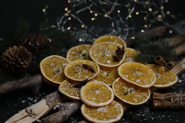 Kurutulmuş portakal kozalakları tarçın köknarı dalları ve yıldız anasonu ahşap doğal sopaların üzerine serilmiş kar ve çelenklerle kaplı karanlık bir arka planda Noel süslemesi. Kart takvimi etiketleri, işaret davetiyesi ilanları için