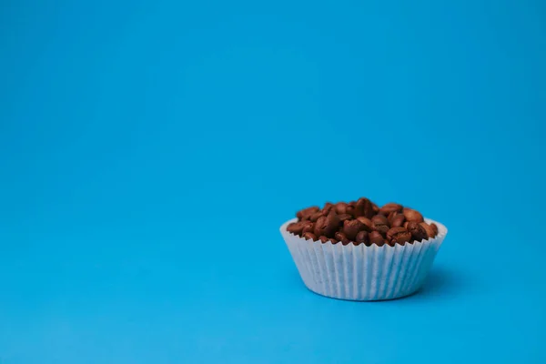 fragrant coffee beans are poured in a cupcake mold on a bright blue background. for splash screens, labels, postcards, signs, announcement menus and more